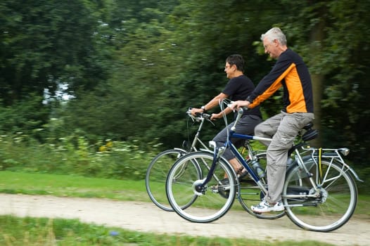 Seniors biking on a sandy path with motion in the picture. Focus is on the woman.