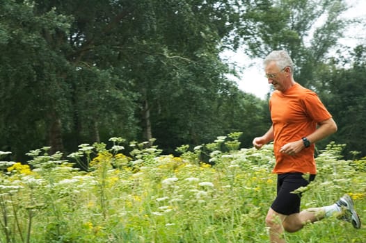 Senior man is running through a field of flowers.