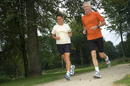Senior couple running through the woods.