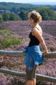 Beautiful woman standing at a fence, looking at a nice heather landscape.