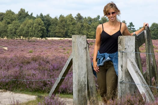 Beautiful woman coming through the fence in a nice heather landscape.