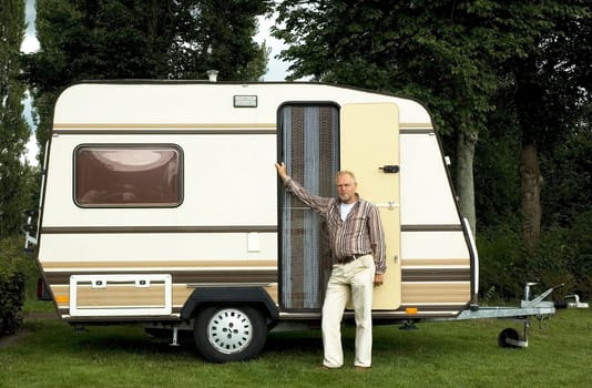 Senior man standing in front of his caravan