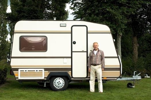 Senior man standing in front of his caravan