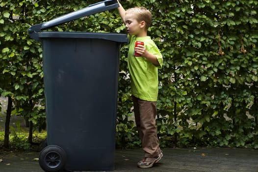 Boy wanting to throw a can in the container, he is learning to be aware that recycling is important.