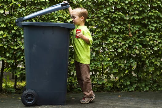 Boy wanting to throw a can in the container, he is learning to be aware that recycling is important.