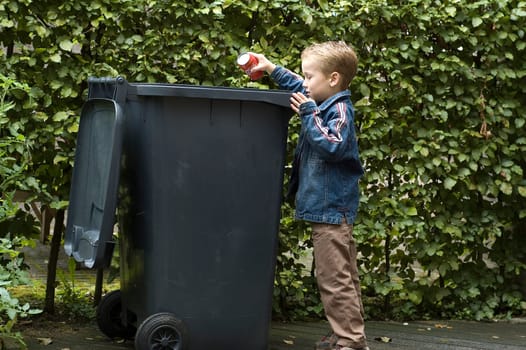 Boy wanting to throw a can in the container, he is learning to be aware that recycling is important.