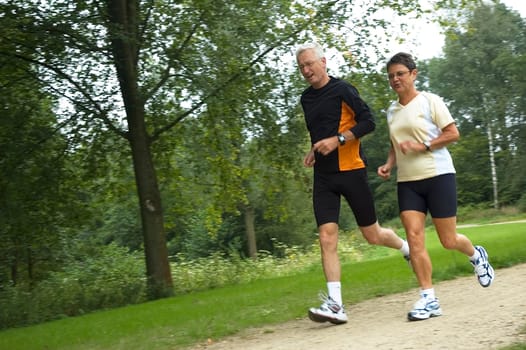 Active senior couple running in the woods.