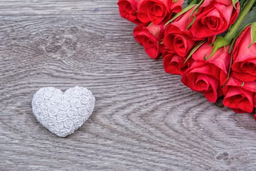White heart and red roses on a wooden background
