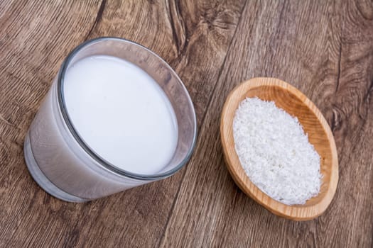 Coconut milk and the dish with grated coconut on a wooden background