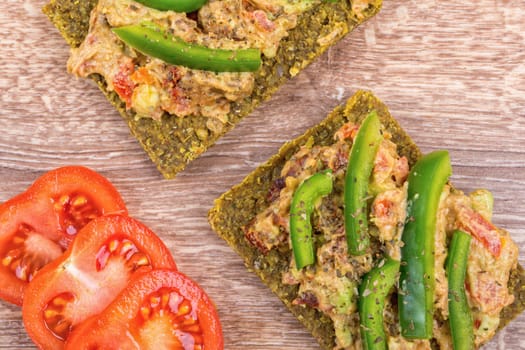 Raw bread with a spread decorated with green pepper and tomatoes