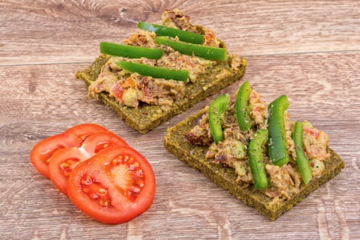 Raw bread with a spread decorated with green pepper and tomatoes