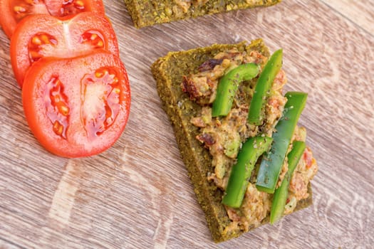 Raw bread with a spread decorated with green pepper and tomatoes