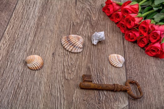 Rusty key, sea shell and red roses on a wooden background