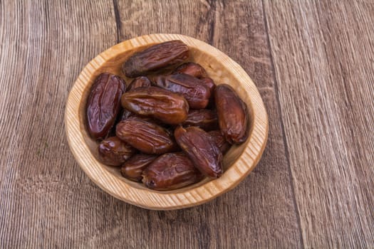 Dried dates in a wooden bowl on a brown wooden background