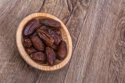 Dried dates in a wooden bowl on a brown wooden background