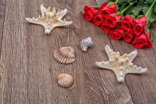 White starfishes, shells and red roses on a wooden background