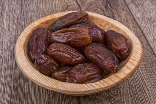 Dried dates in a wooden bowl on a brown wooden background