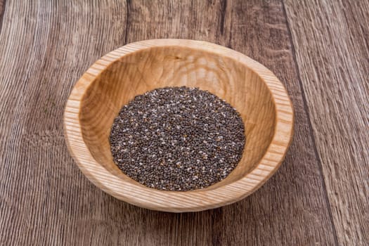 Chia seeds in a wooden bowl on a brown wooden background