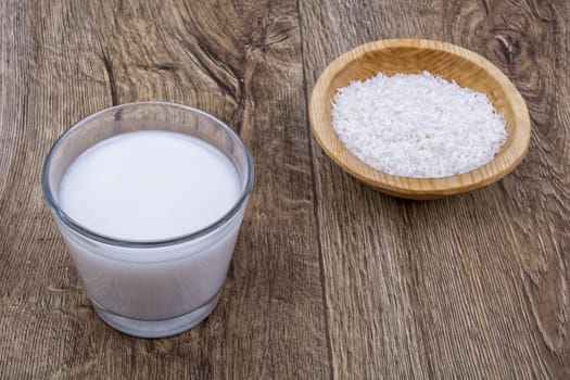 Coconut milk and the dish with grated coconut on a wooden background