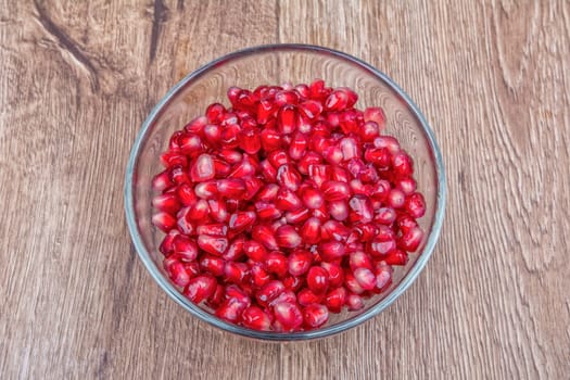 Fresh organic pomegranate seeds in a bowl on a wooden background