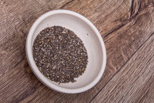 Chia seeds in a bowl on a brown wooden background