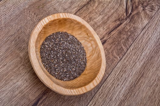Chia seeds in a wooden bowl on a brown wooden background