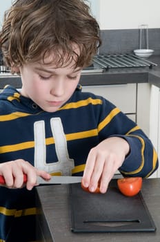 Boy cutting a tomato, getting ready to cook.