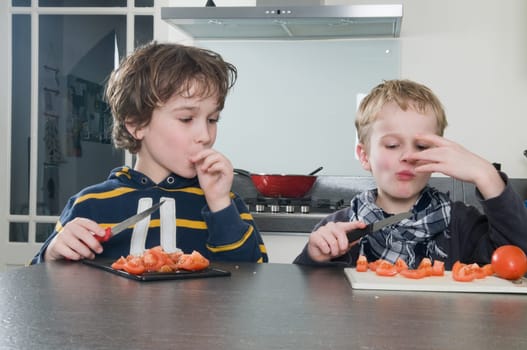Two boys tasting the just cutted tomatos, used for cooking.
