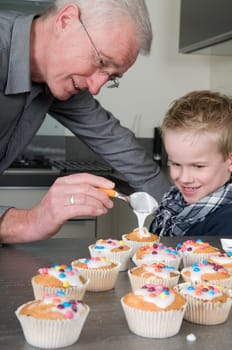 Grandpa and child are decorating the just baked cupcakes