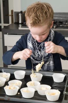 Kid filling the cakecups with the dough, for baking cakes.
