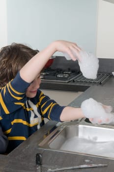 Boy having fun with soap while doing the dishes