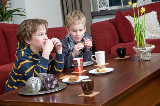Two brothers drinking and eating something in a livingroom