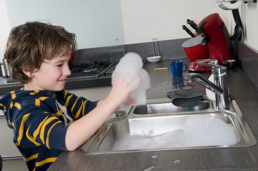 Boy having fun with soap while doing the dishes
