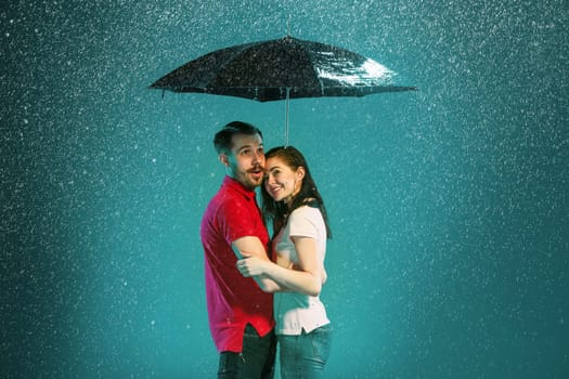 The loving couple in the rain with umbrella on a turquoise background