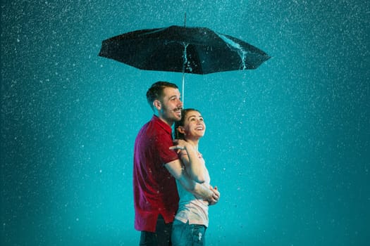 The loving couple in the rain with umbrella on a turquoise background