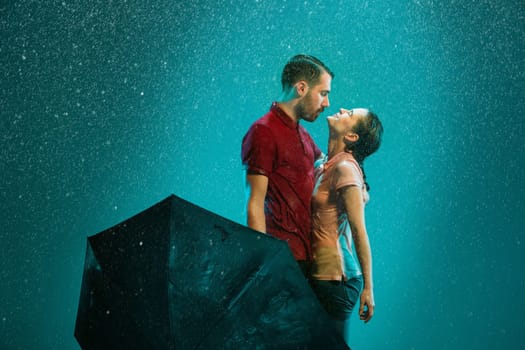 The loving couple in the rain with umbrella on a turquoise background