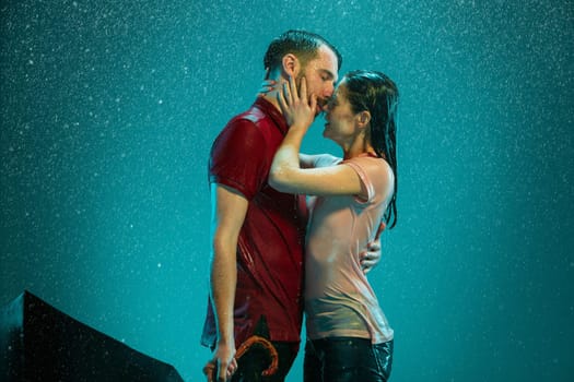 The loving couple in the rain with umbrella on a turquoise background