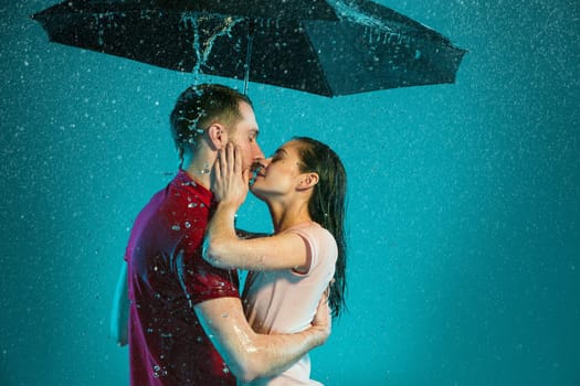 The loving couple in the rain with umbrella on a turquoise background