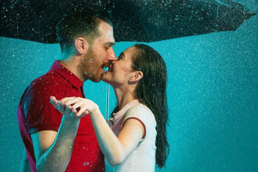 The loving couple in the rain with umbrella on a turquoise background