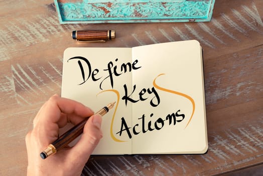 Retro effect and toned image of a woman hand writing a note with a fountain pen on a notebook. Handwritten text Define Key Actions as business concept image