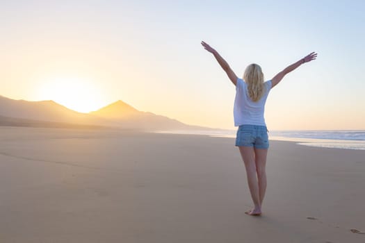 Free woman enjoying freedom feeling happy at beach at sunrise. Serene relaxing woman in pure happiness and elated enjoyment with arms raised outstretched up.