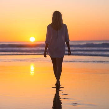 Woman walking on sandy beach in sunset leaving footprints in the sand. Beach, travel, concept. Copy space. Vertical composition.