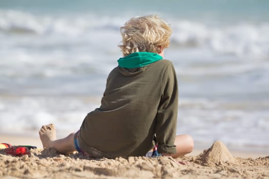 Cute child playing with beach toys on the sand. Rear view.