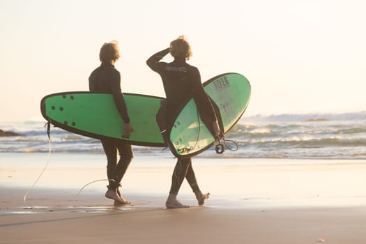 Male surfers on sandy beach with the surfboard in sunset.