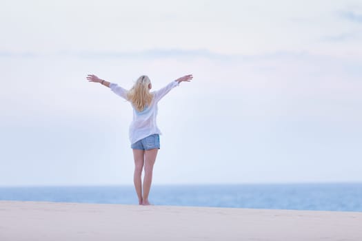 Relaxed woman enjoying freedom feeling happy at beach in the morning. Serene relaxing woman in pure happiness and elated enjoyment with arms raised outstretched up.
