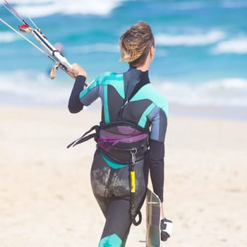 Sporty fit female kiteboarder walking in water with lunched kite and holding her board to start kiteboarding session.