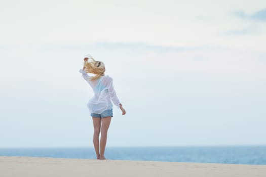 Meditative, sensual blonde woman wearing white loose casual shirt on vacations, looking at horizon, enjoying peaceful early morning.