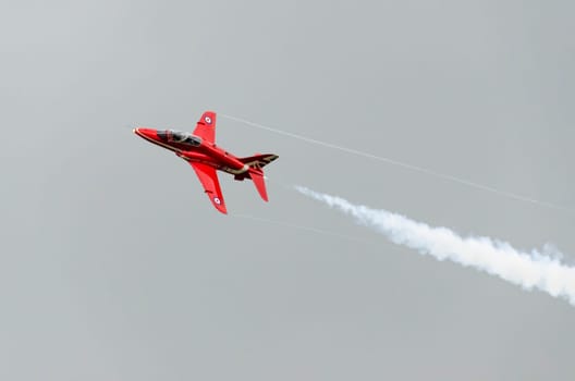 A single Red Arrow aeroplane in flight with white vapour emitting from it's tail end