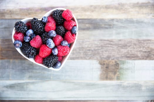 Healthy fresh fruit salad with strawberries, blackberries, blueberries and raspberries. in heart shape bowl.