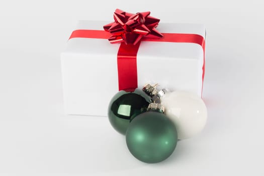Christmas present in white paper with red ribbon and bow, green and white Christmas balls, isolated on white background